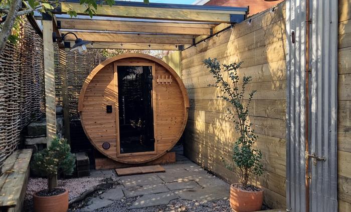 A round wooden barrel sauna with a glass door and benches for sitting on and an outdoor shower